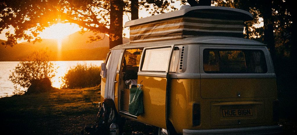 En klassisk gul campervan med hævetag parkeret ved en sø i solnedgangen, der symboliserer friheden ved vanlife.